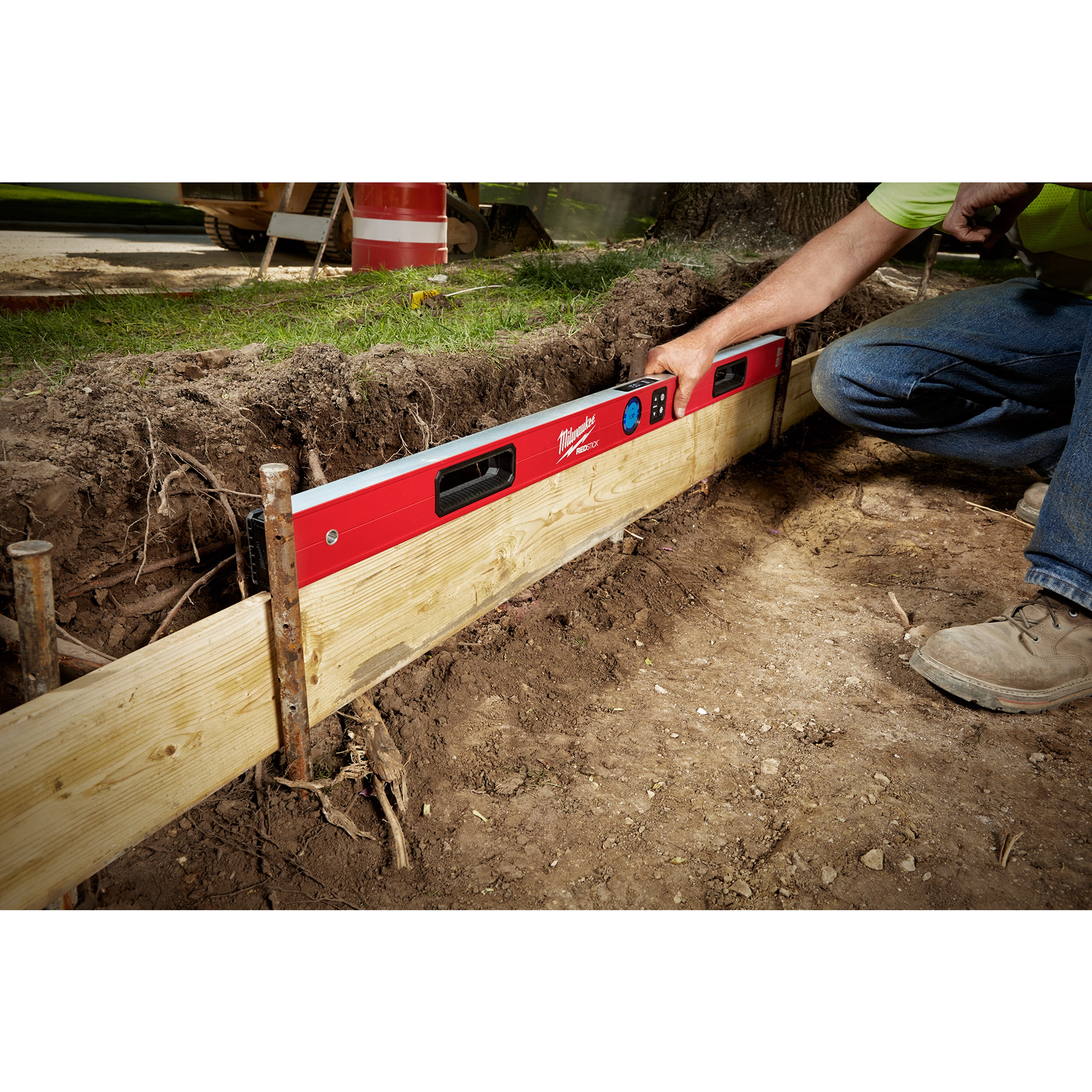A person is using the Milwaukee REDSTICK Digital Level with PINPOINT Measurement Technology to level a wooden framework in a construction area.
