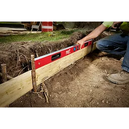 A person is using the Milwaukee REDSTICK Digital Level with PINPOINT Measurement Technology to level a wooden framework in a construction area.