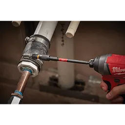 Close-up of SHOCKWAVE Impact Locking Bit Holder attached to a red power drill, tightening a metal fitting on a pipe assembly.