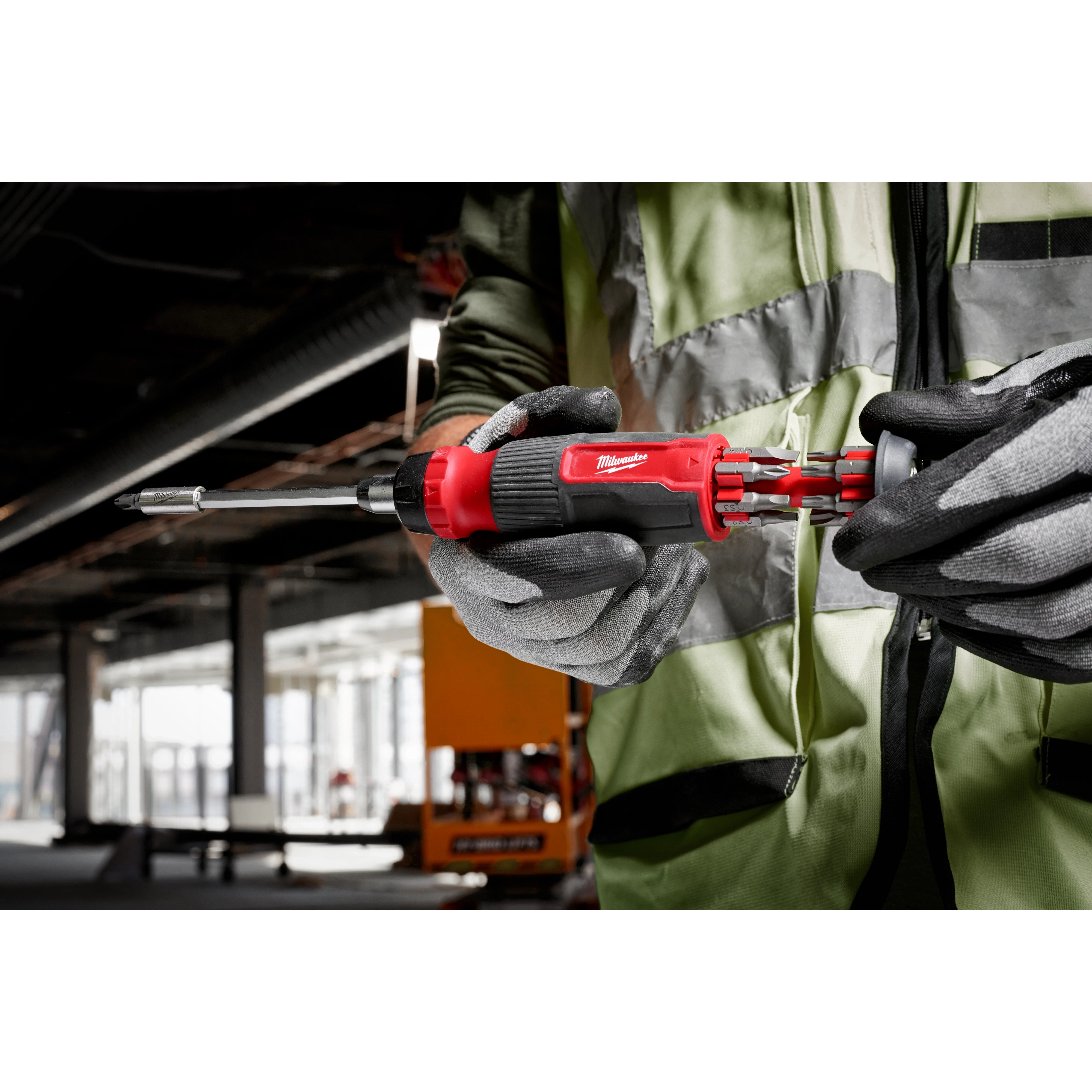 Person wearing gloves and a safety vest holds a 14-in-1 Ratcheting Multi-Bit Screwdriver with interchangeable bits displayed.