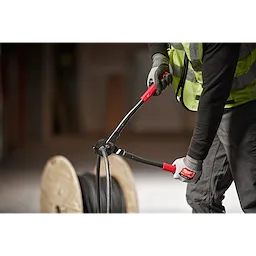 Person using the 17" Utility Cable Cutter to cut thick black cables, wearing a high-visibility vest and gloves, with a cable spool nearby.