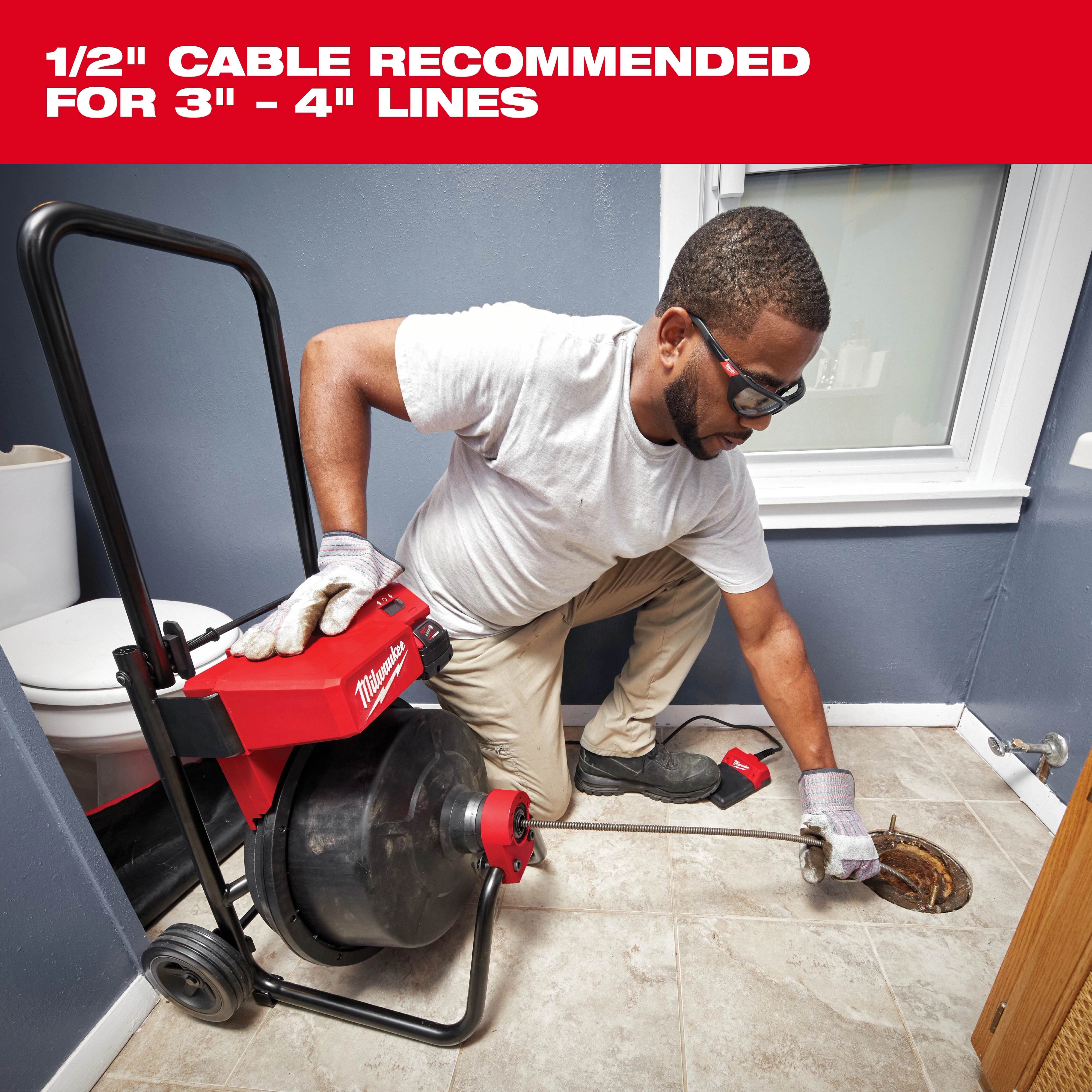 A person kneels on a bathroom floor using a Milwaukee drain cleaning machine with a 1/2" cable, recommended for 3" to 4" lines.