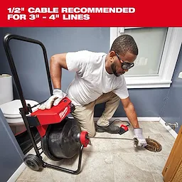 A person kneels on a bathroom floor using a Milwaukee drain cleaning machine with a 1/2" cable, recommended for 3" to 4" lines.
