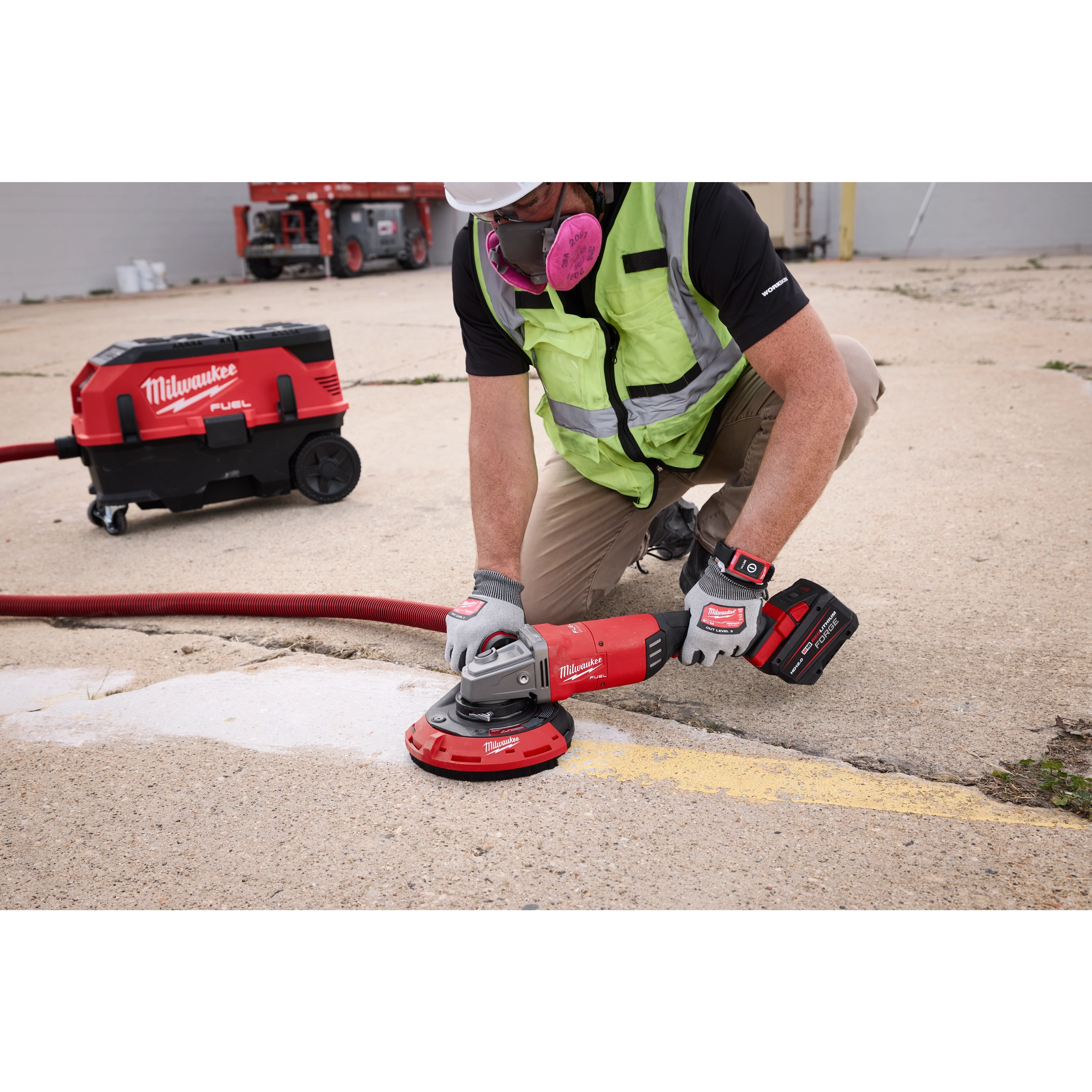 A worker uses a Milwaukee 7"/9" Surface Grinding Dust Shroud attached to a grinder on a concrete surface. A vacuum dust collector is connected to a hose to efficiently manage debris.