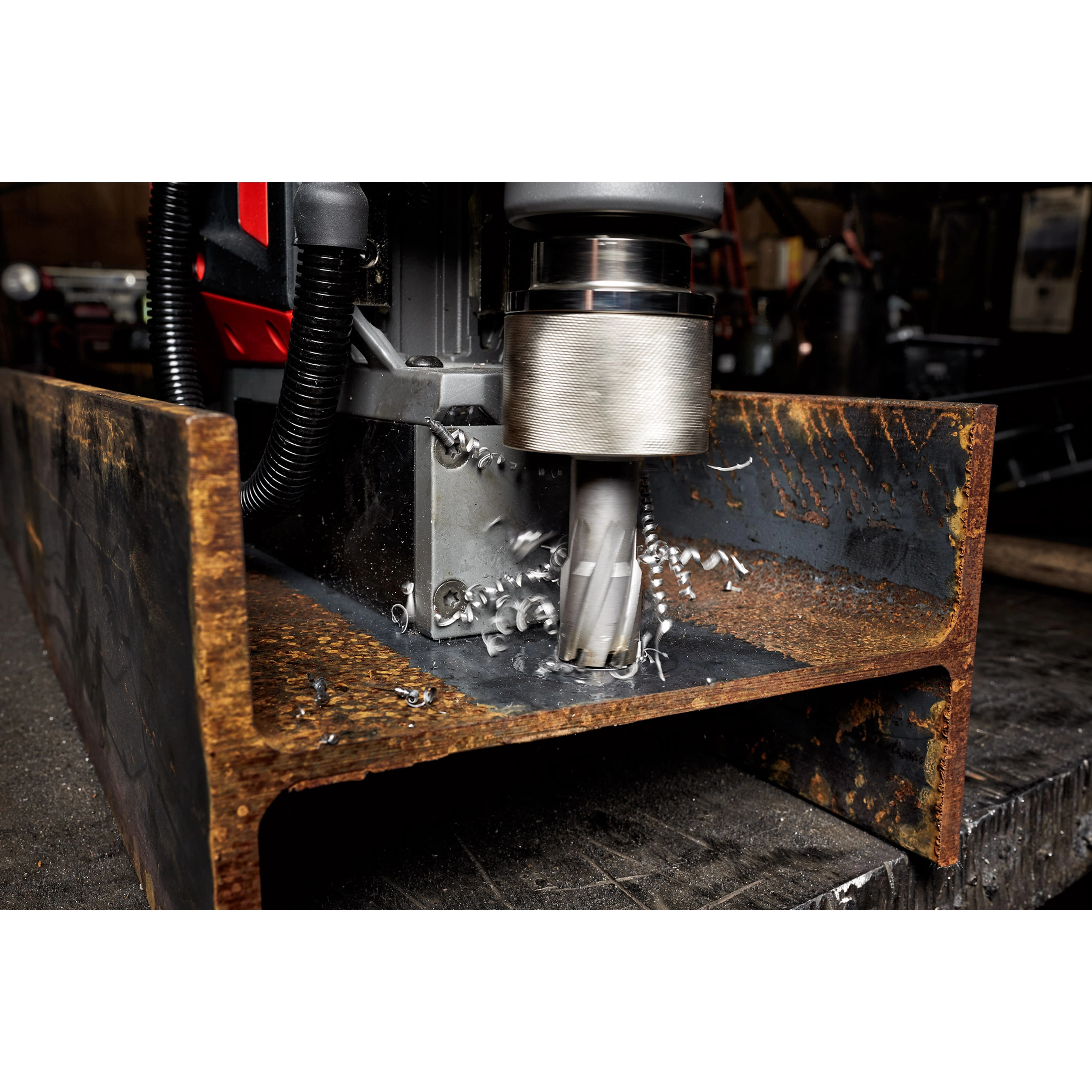 Annular Cutter drilling into a thick, rusted metal beam, producing metal shavings. The cutter is attached to industrial machinery.