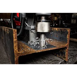 Annular Cutter drilling into a thick, rusted metal beam, producing metal shavings. The cutter is attached to industrial machinery.
