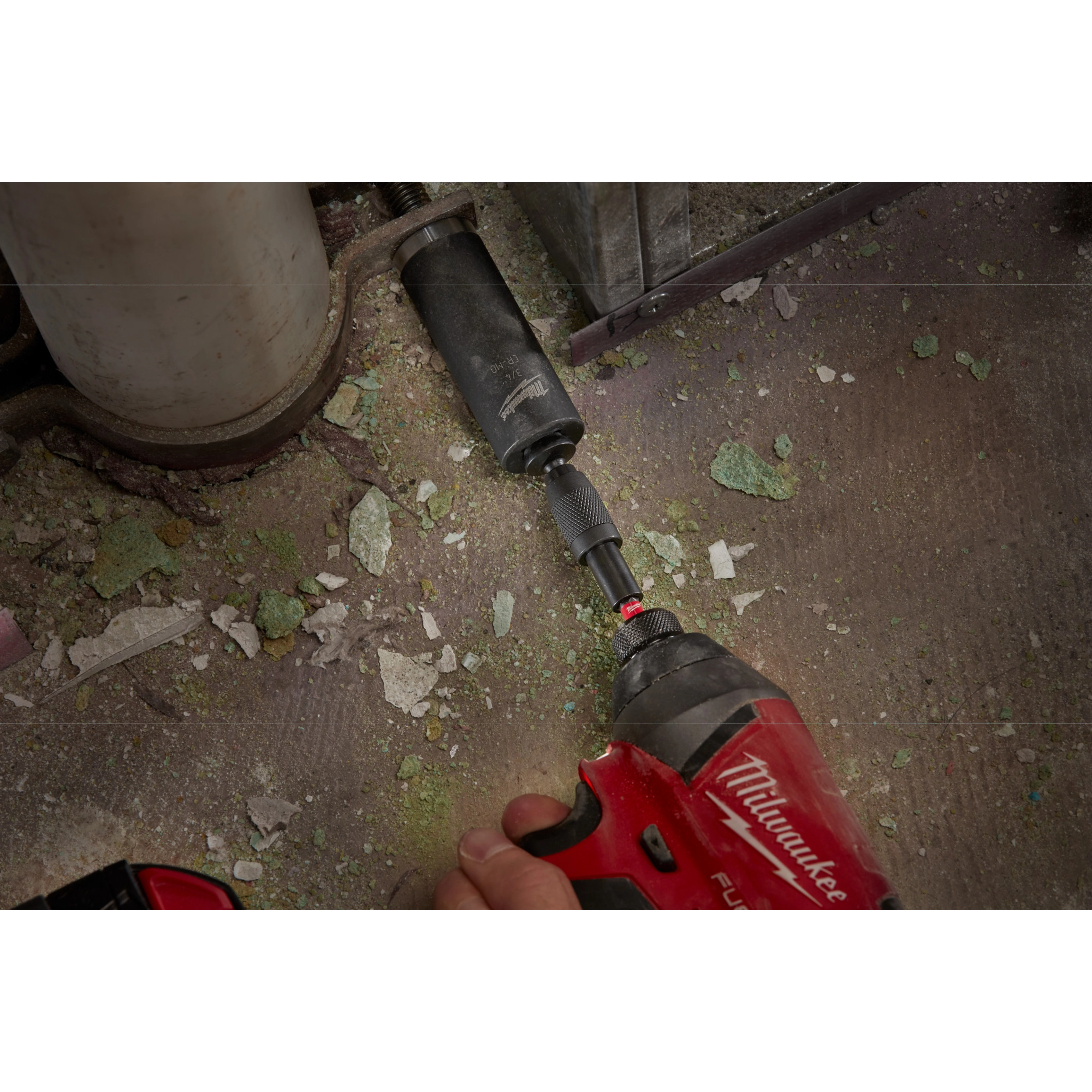 A red power drill with the SHOCKWAVE Impact Locking Bit Holder is being used to screw a black attachment onto a surface with debris.