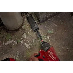 A red power drill with the SHOCKWAVE Impact Locking Bit Holder is being used to screw a black attachment onto a surface with debris.