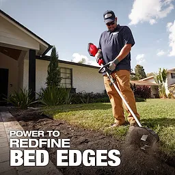 A person is using a power tool to edge a garden bed beside a house with a white exterior. The text overlay reads, "POWER TO REDEFINE BED EDGES." The tool is kicking up soil while creating a neat border.