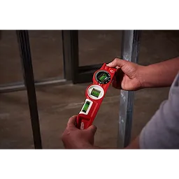 A person holds a red Block Torpedo Level, aligning framing metal studs. The level has three bubble vials and an angle finder.