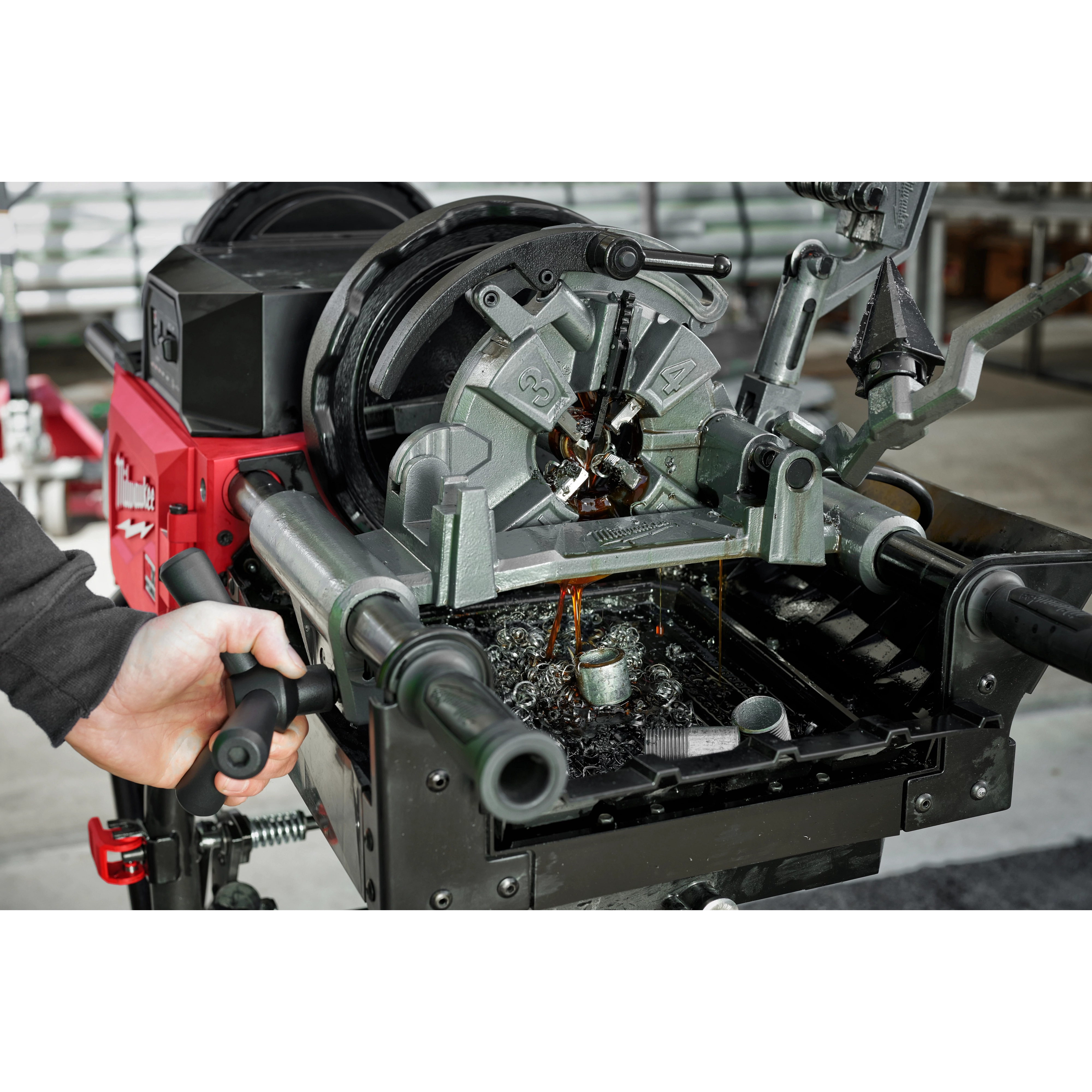 Person operating MX FUEL Pipe Threading Machine with metal pipes and oil shavings visible, showcasing threading process.