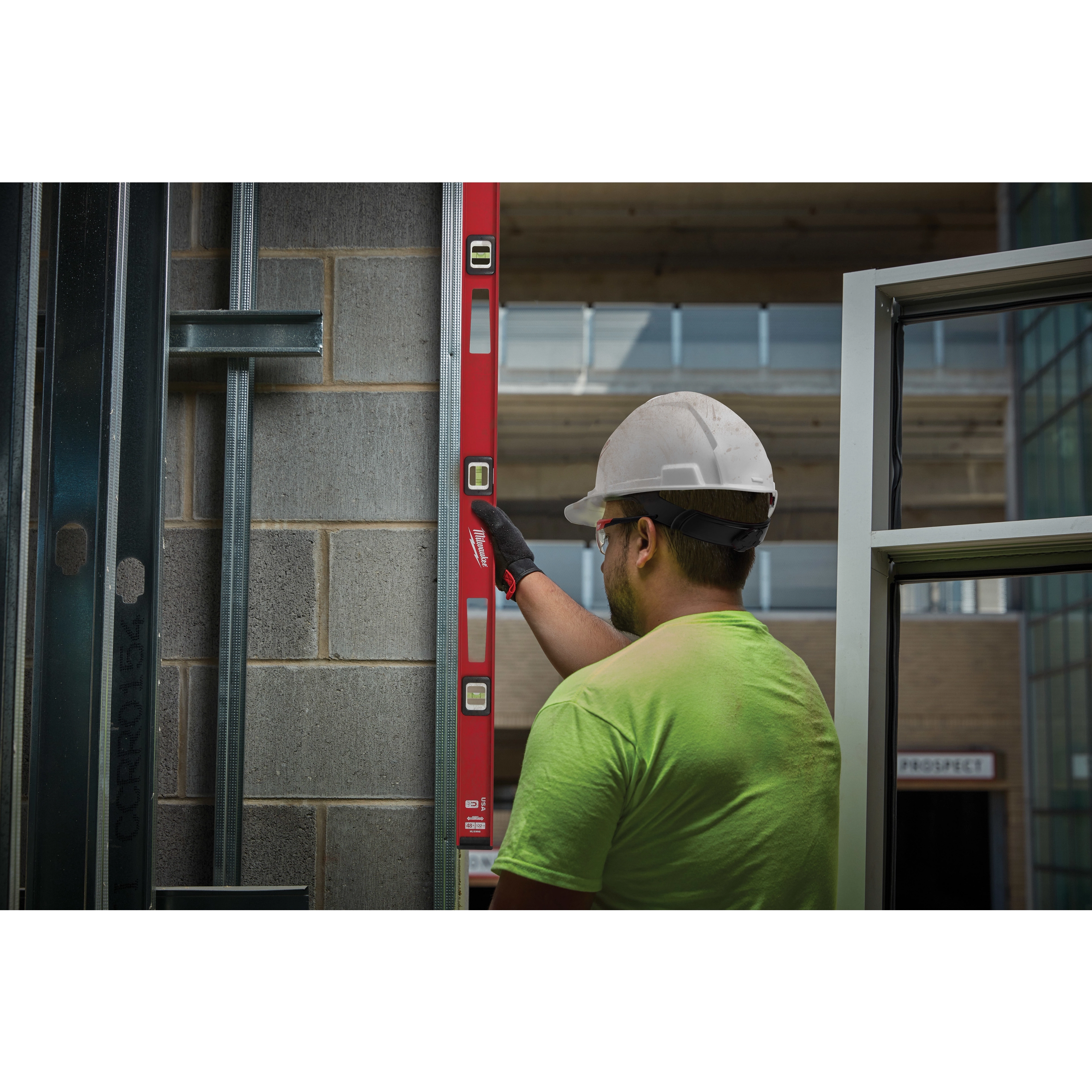 A construction worker uses a Milwaukee 48" Magnetic I-Beam Level to ensure a vertical structure is straight against a brick wall.