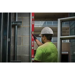 A construction worker uses a Milwaukee 48" Magnetic I-Beam Level to ensure a vertical structure is straight against a brick wall.