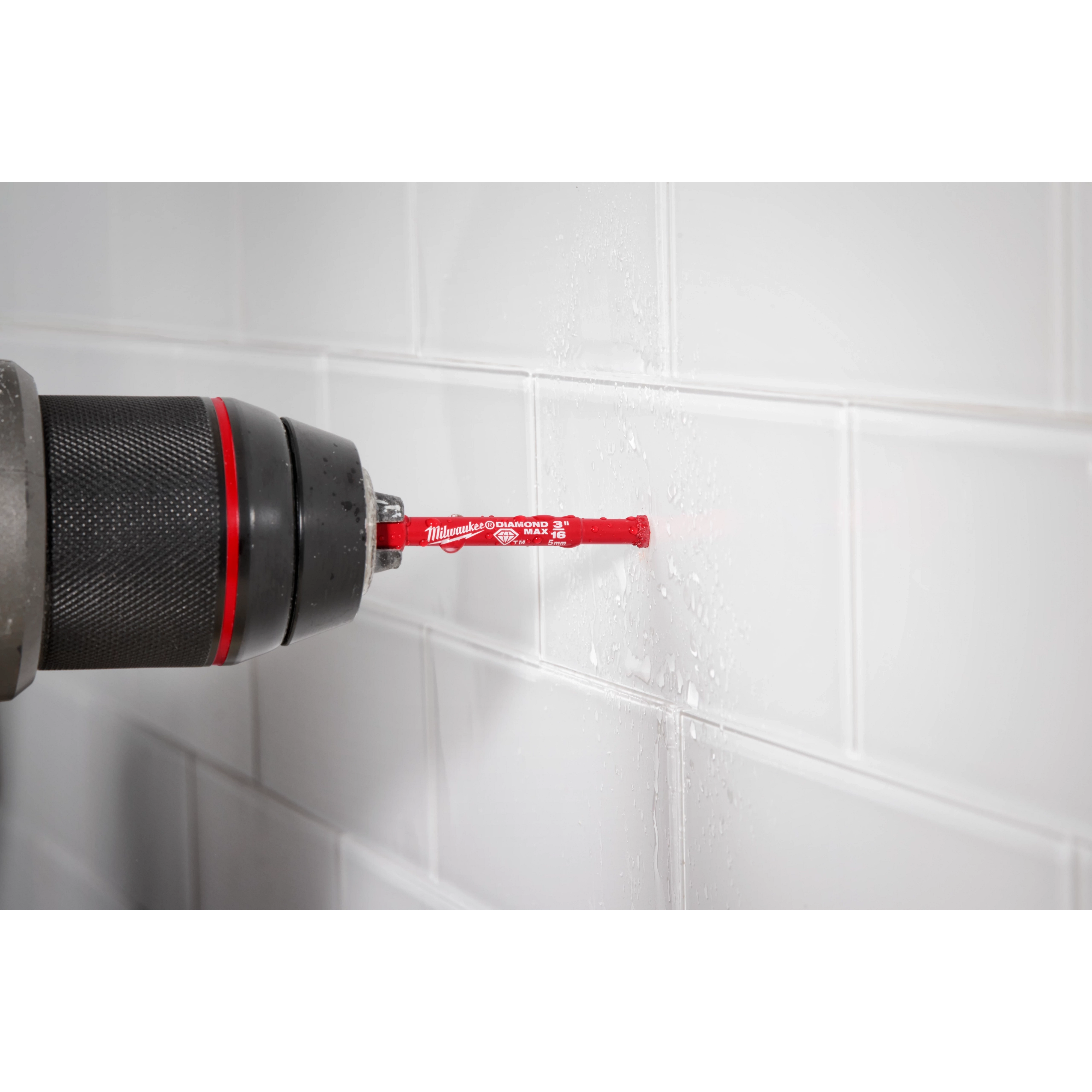 A Milwaukee® 3/16" DIAMOND MAX™ Hole Saw Bit fitted in a drill is shown drilling into white, glossy ceramic tiles on a wall. The red color of the bit and the brand label are clearly visible, with water droplets indicating active drilling.