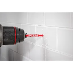 A Milwaukee® 3/16" DIAMOND MAX™ Hole Saw Bit fitted in a drill is shown drilling into white, glossy ceramic tiles on a wall. The red color of the bit and the brand label are clearly visible, with water droplets indicating active drilling.