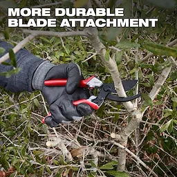 A gloved hand is using a 1" Pruner with a red handle to cut a branch from a bush. The text "MORE DURABLE BLADE ATTACHMENT" is displayed at the top of the image.
