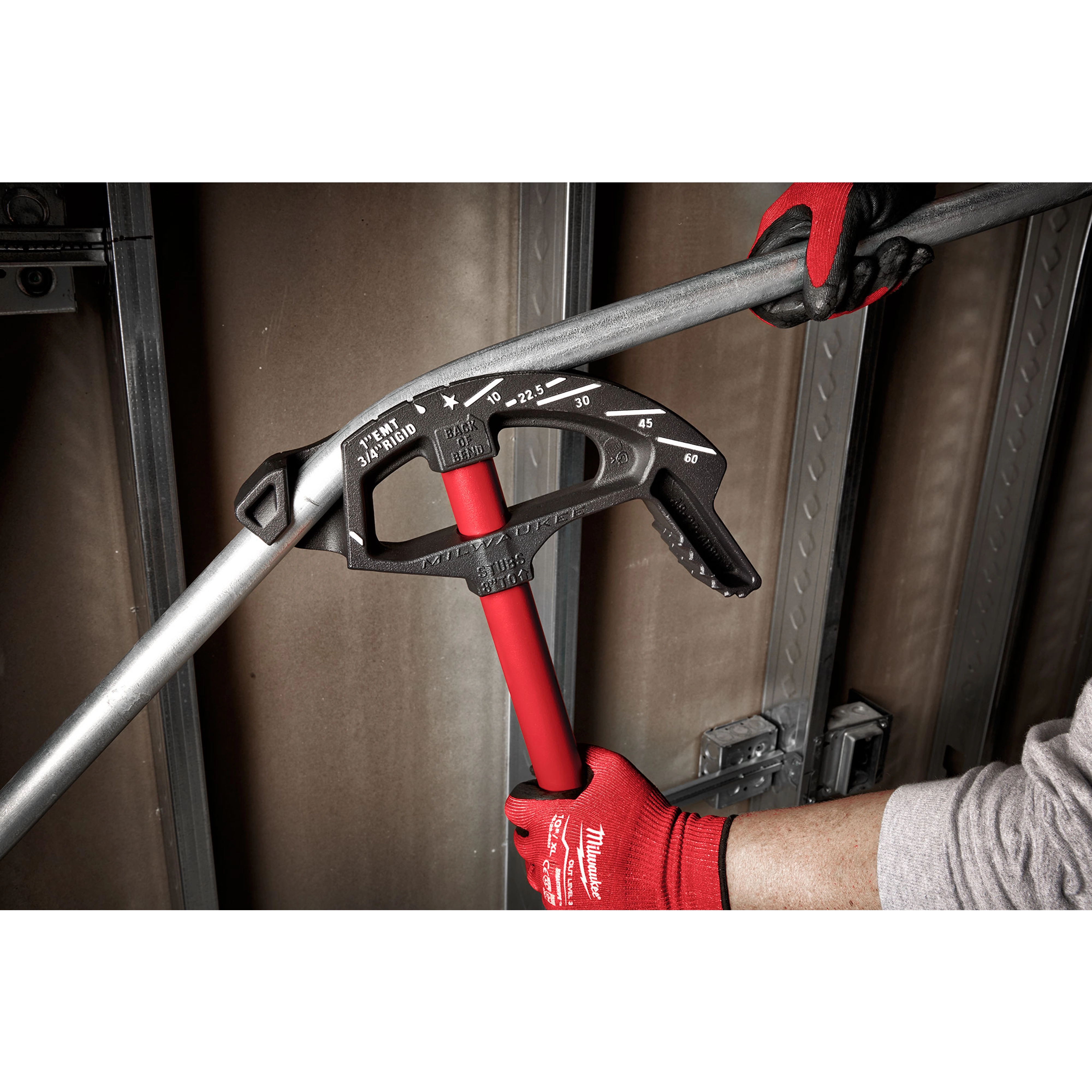 1" EMT Iron Conduit Bender with red handle, held by gloved hands, shown bending a metal conduit pipe in an industrial setting.