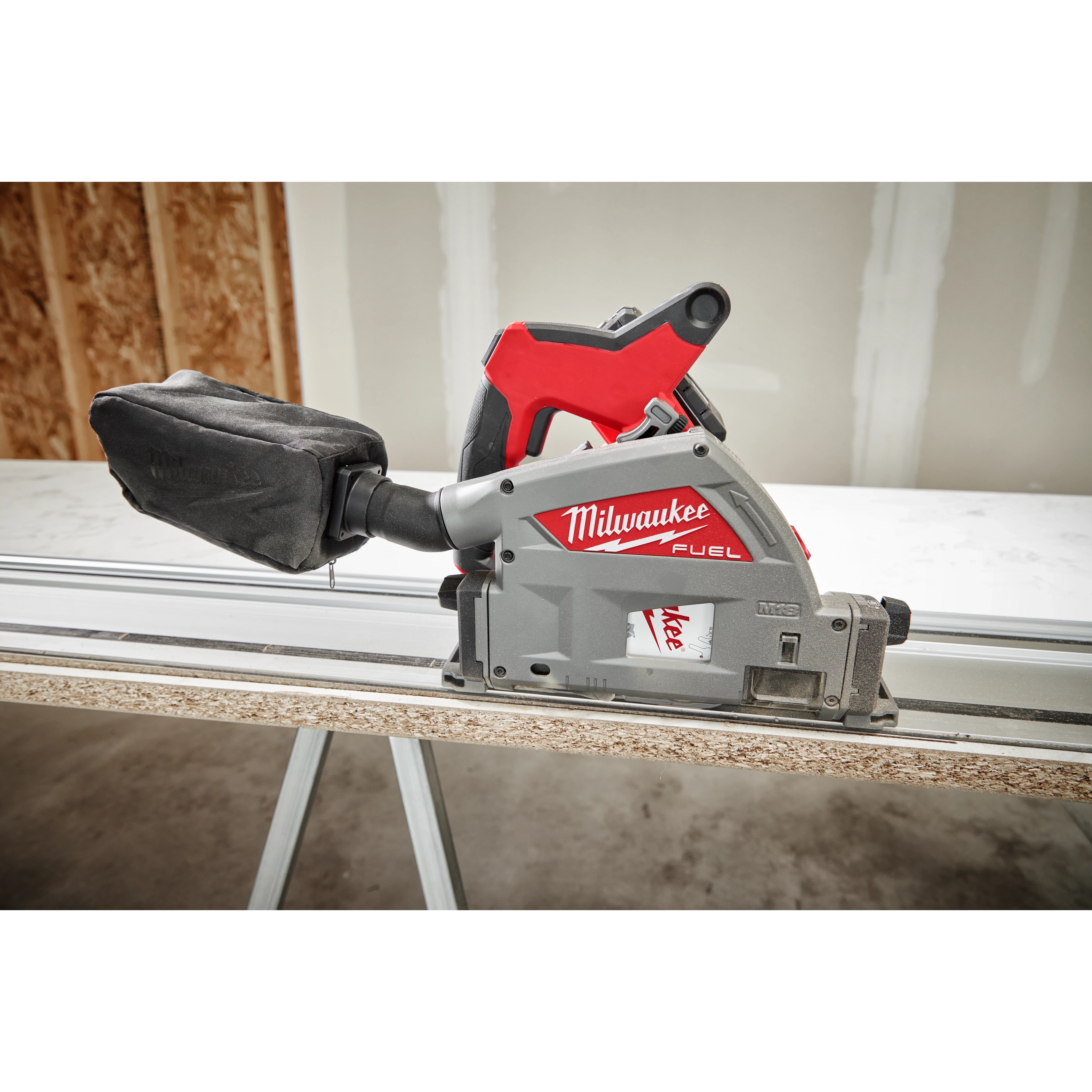 Milwaukee Fuel 6-1/2" 52T Laminate Track Saw cutting a piece of laminated wood on a workbench, with a dust bag attached.