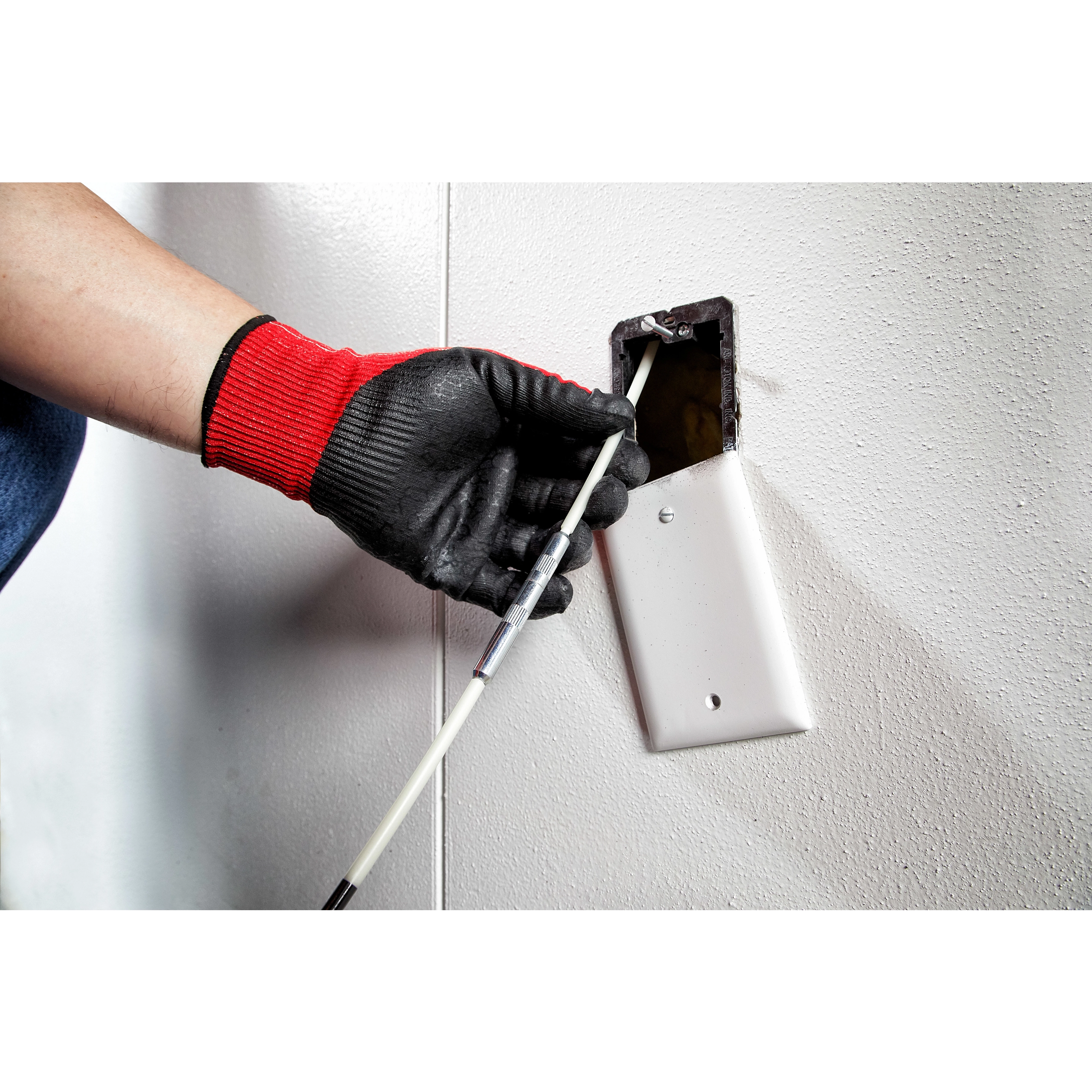 A person wearing red and black gloves guides the 5' High Flex Fish Stick through a wall outlet opening.