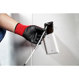 A person wearing red and black gloves guides the 5' High Flex Fish Stick through a wall outlet opening.