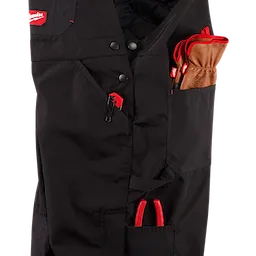 Close-up of the black FREEFLEX Insulated Bib Overalls, showcasing multiple pockets holding gloves, pliers, and a red zipper pull.