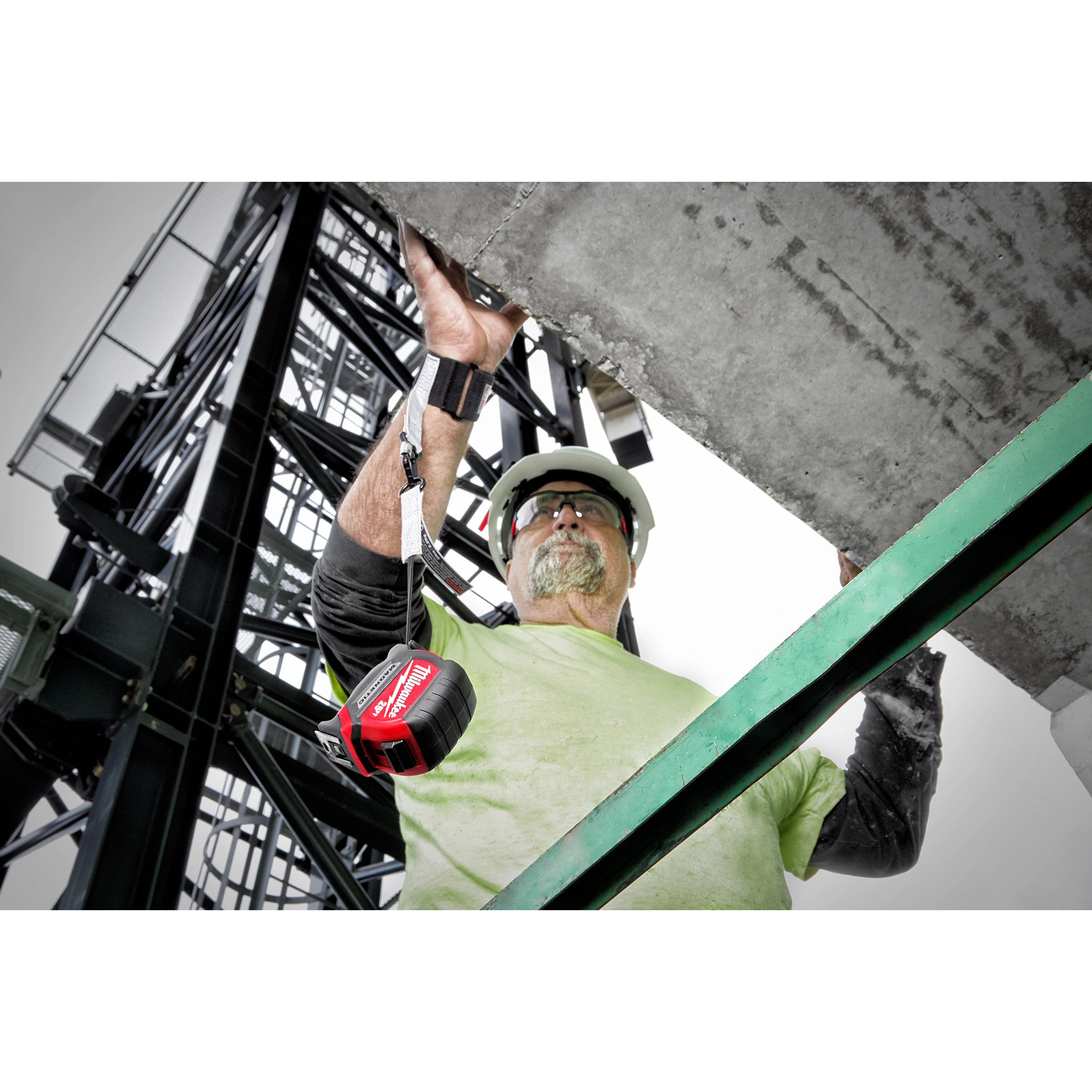 A worker wearing a Quick-Connect Wrist Lanyard attached to a red battery pack while securing a concrete structure on a construction site.