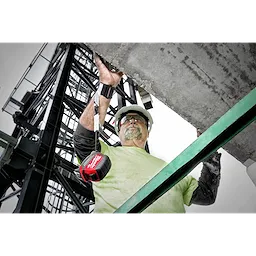 A worker wearing a Quick-Connect Wrist Lanyard attached to a red battery pack while securing a concrete structure on a construction site.