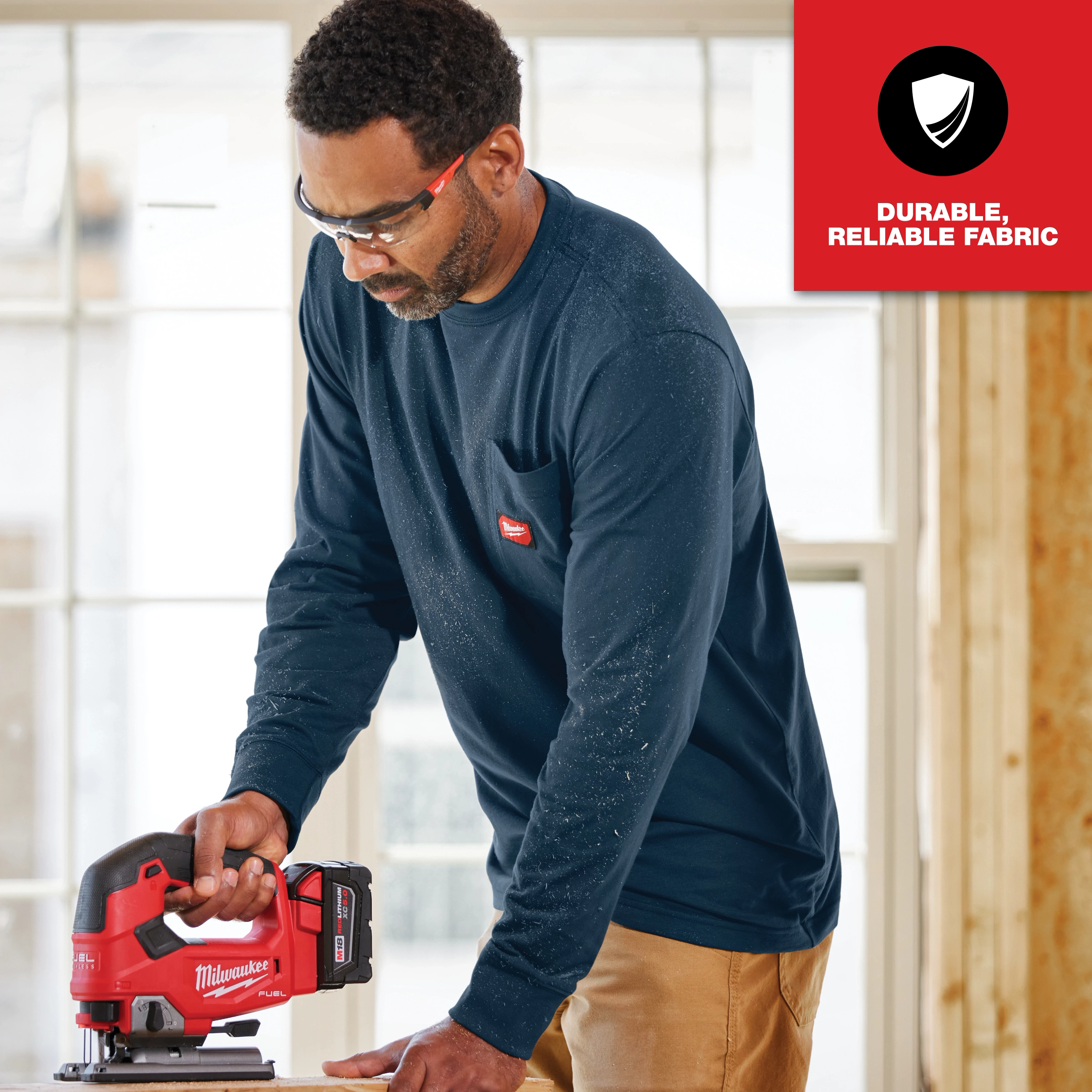 Man wearing GRIDIRON Pocket T-Shirt - Long Sleeve in navy blue, operating a red and black power tool, with a "Durable, Reliable Fabric" label.