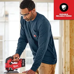 Man wearing GRIDIRON Pocket T-Shirt - Long Sleeve in navy blue, operating a red and black power tool, with a "Durable, Reliable Fabric" label.