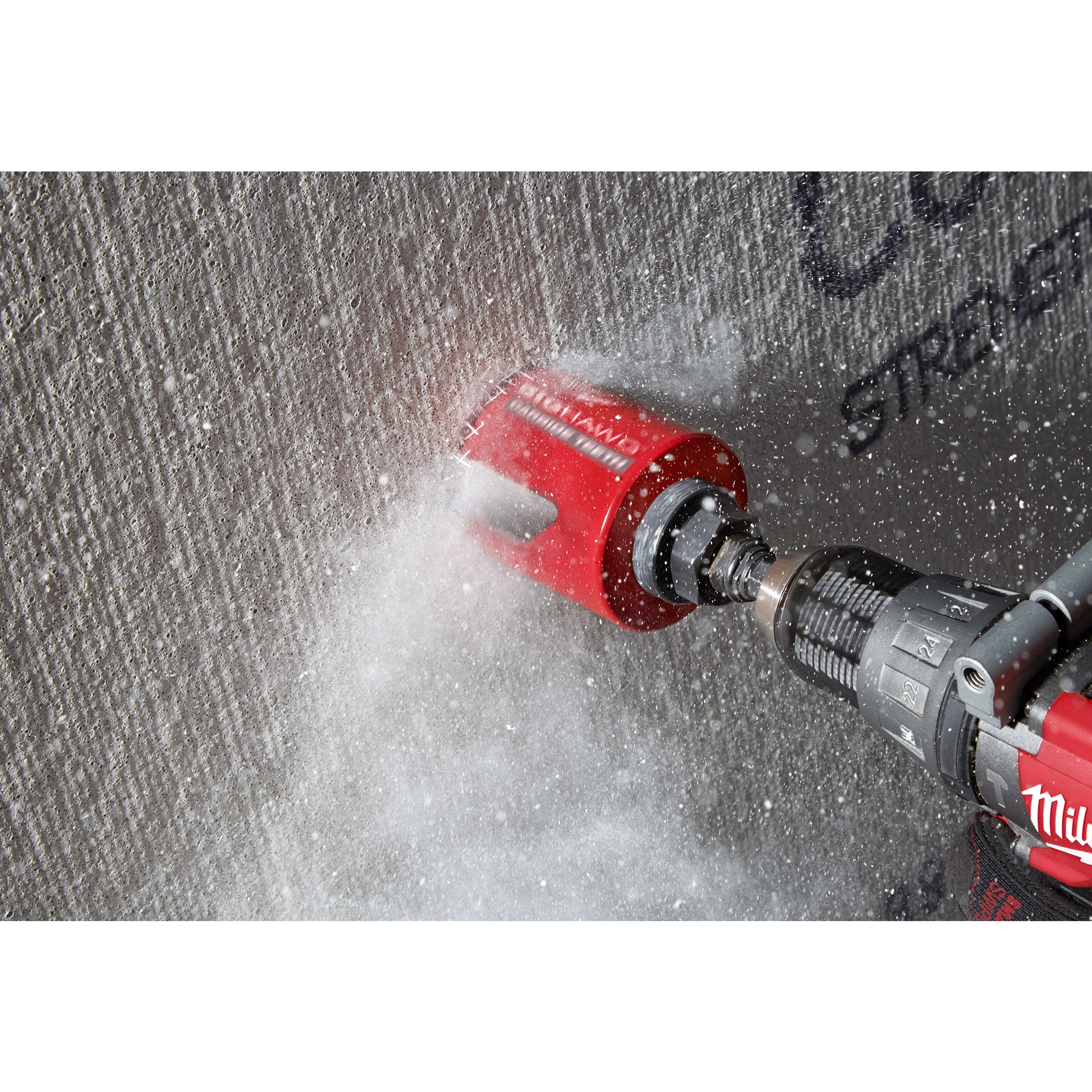 The 2-9/16" BIG HAWG™ with Carbide Teeth is shown in action, cutting through a concrete wall. The red hole saw is attached to a power drill, generating dust and debris as it operates.