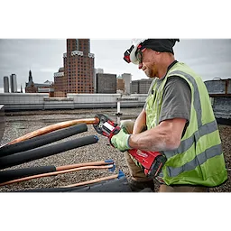 A worker uses RLS ACR Press Jaws for M18 FORCE LOGIC Press Tools on copper pipes, with a cityscape in the background.