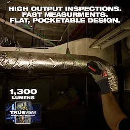 Worker aims Milwaukee Rechargeable Flat Flashlight w/ Green Laser at ductwork in a dim industrial space.