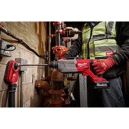 Person using the M18 FUEL 1-1/4" SDS Plus D-Handle Rotary Hammer with ONE-KEY on a concrete wall with red plumbing in the background.