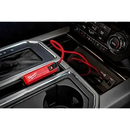 Milwaukee REDLITHIUM™ USB Charger and Portable Power Source Kit, with a red design, is connected to a USB port inside a car. The compact charger is placed near the gear shift with a red cable attached, highlighting its ease of use for charging devices on the go.