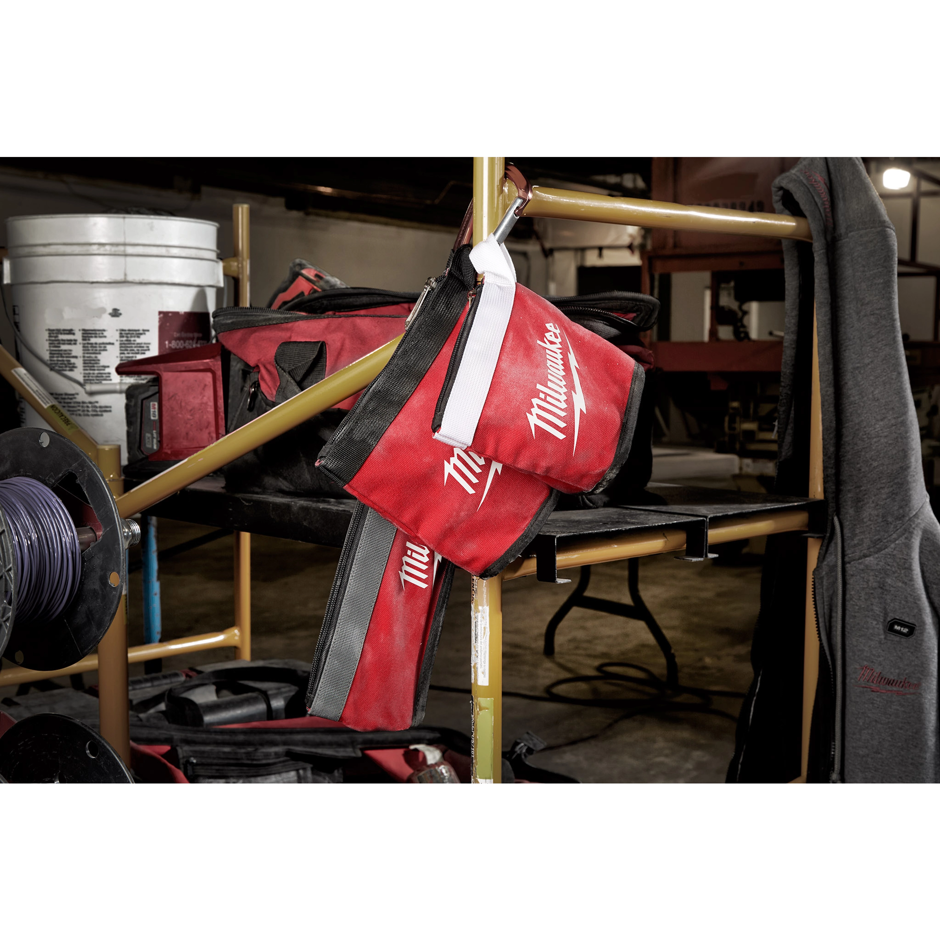 Red and black Zipper Pouch with a white zipper hanging on a metal shelf in a workshop setting, surrounded by tools and equipment.