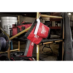 Red and black Zipper Pouch with a white zipper hanging on a metal shelf in a workshop setting, surrounded by tools and equipment.