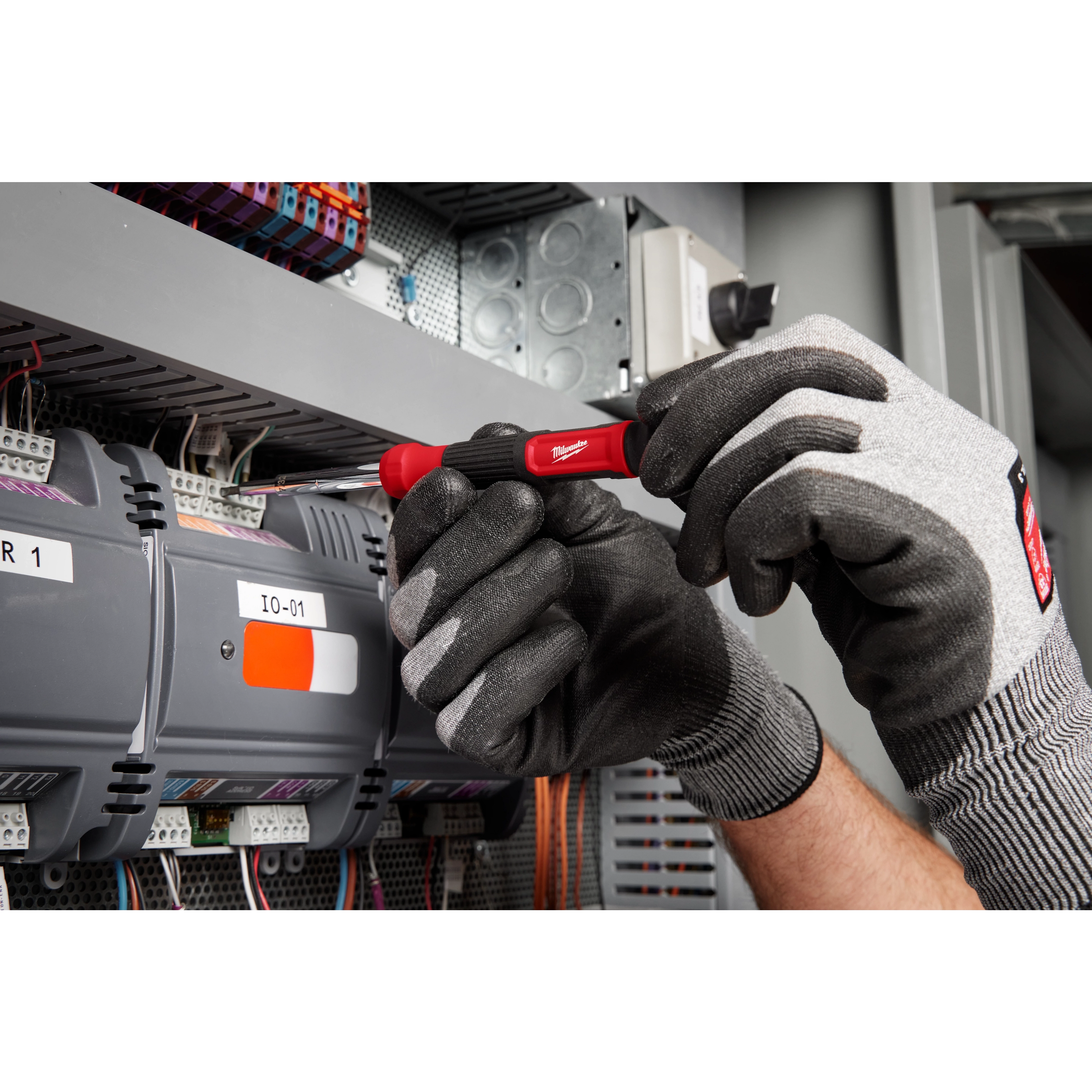 A technician uses the 14-in-1 Precision Multi-Bit Screwdriver to work on an electrical panel while wearing grey work gloves.
