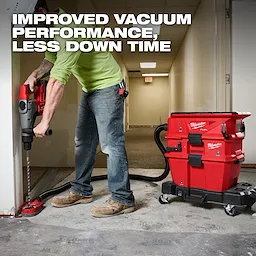 A construction worker uses a Milwaukee drill linked to a red NEXUS™ Dedicated Filter Cleaner. The cleaner is attached to hoses, ensuring improved vacuum performance with less downtime. The cleaner is positioned on wheels for easy mobility in a hallway setting. Text reads "Improved vacuum performance, less down time."