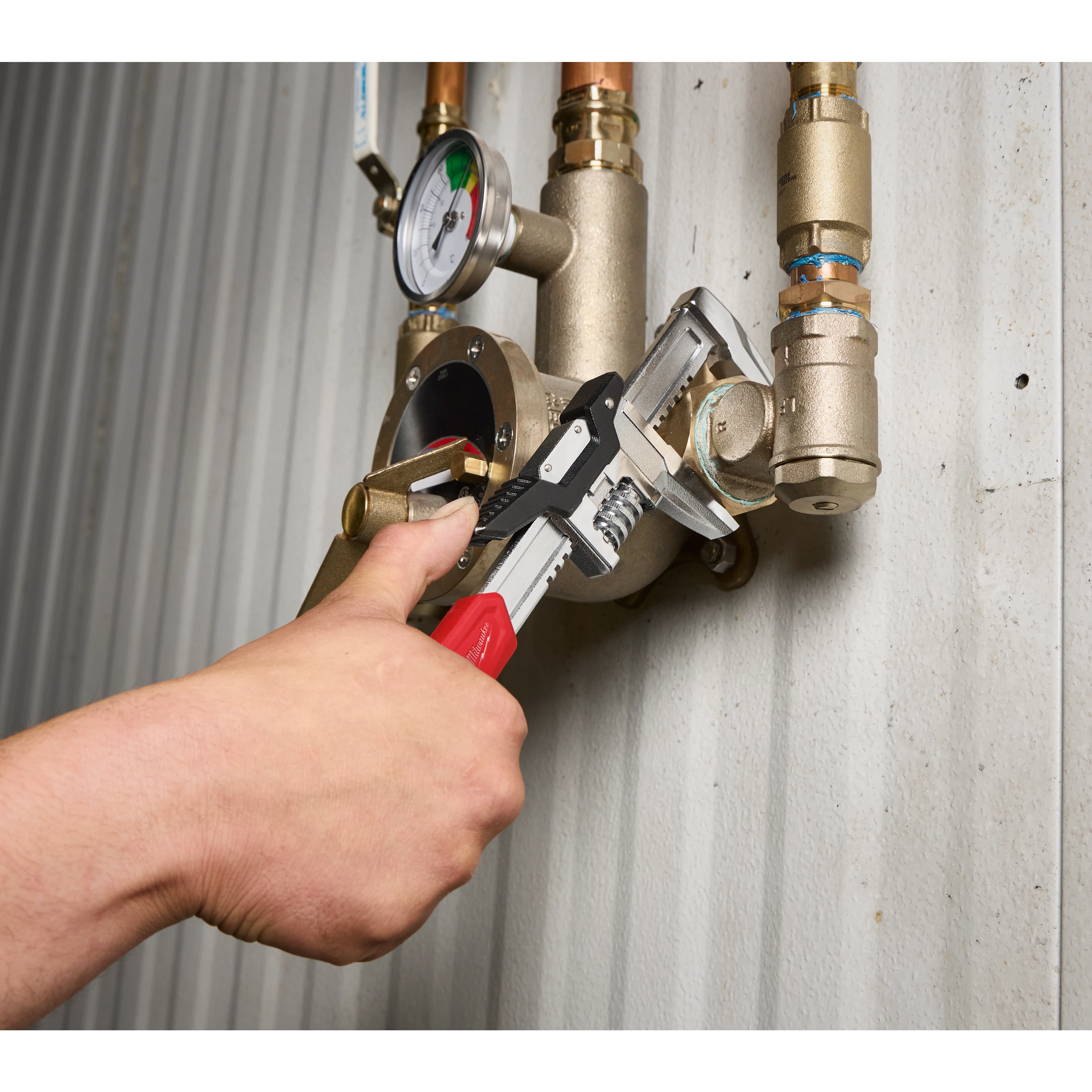 12” Quick Adjust Smooth Jaw Wrench gripping a pipe fitting on a wall-mounted valve and gauge assembly.