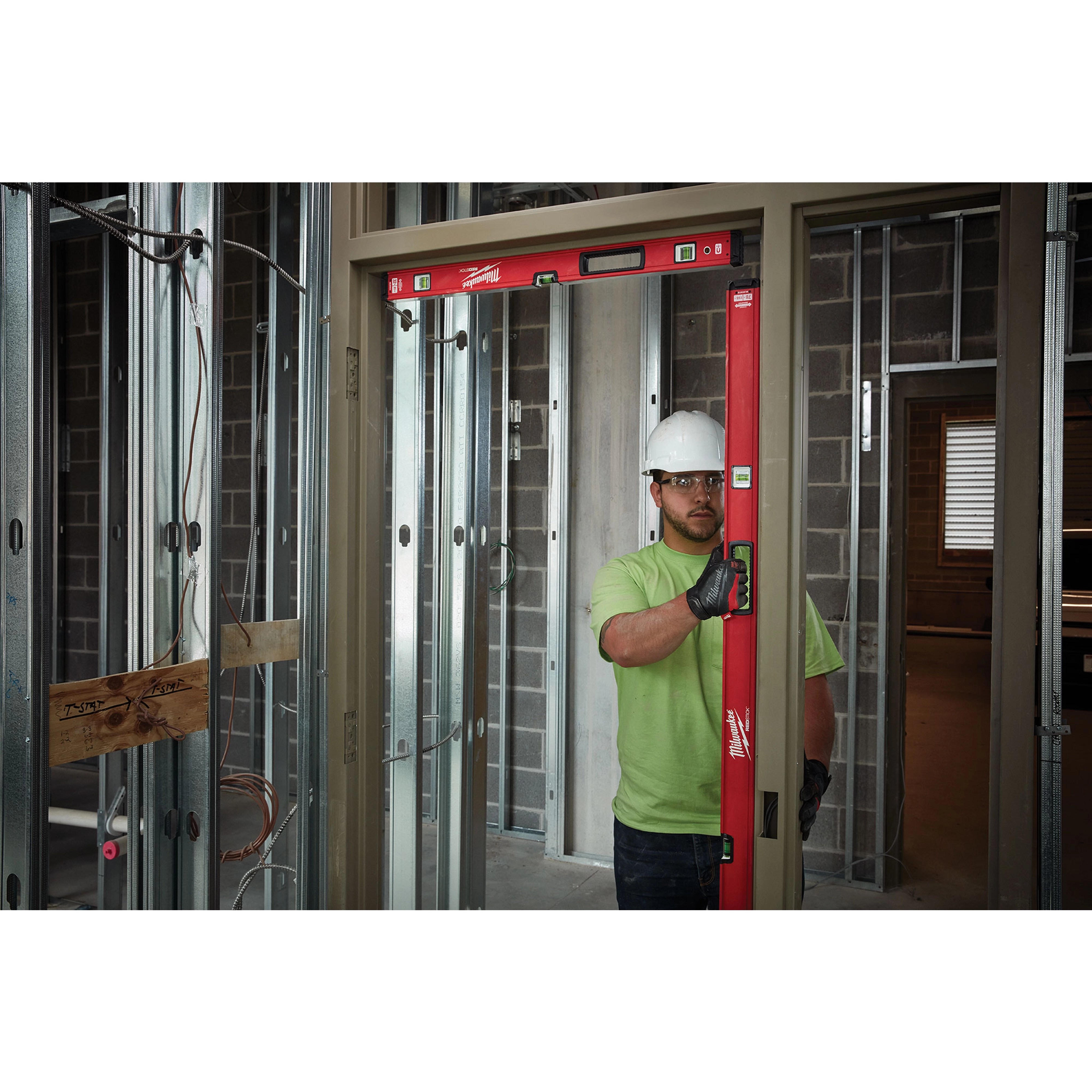 Construction worker using a REDSTICK%20Level to check the alignment of a door frame in a partially built room with metal studs.