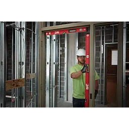 Construction worker using a REDSTICK%20Level to check the alignment of a door frame in a partially built room with metal studs.
