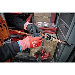 Person wearing Cut Level 2 Winter Dipped Gloves - L, adjusting a ratchet strap inside a workshop with toolboxes and equipment nearby.