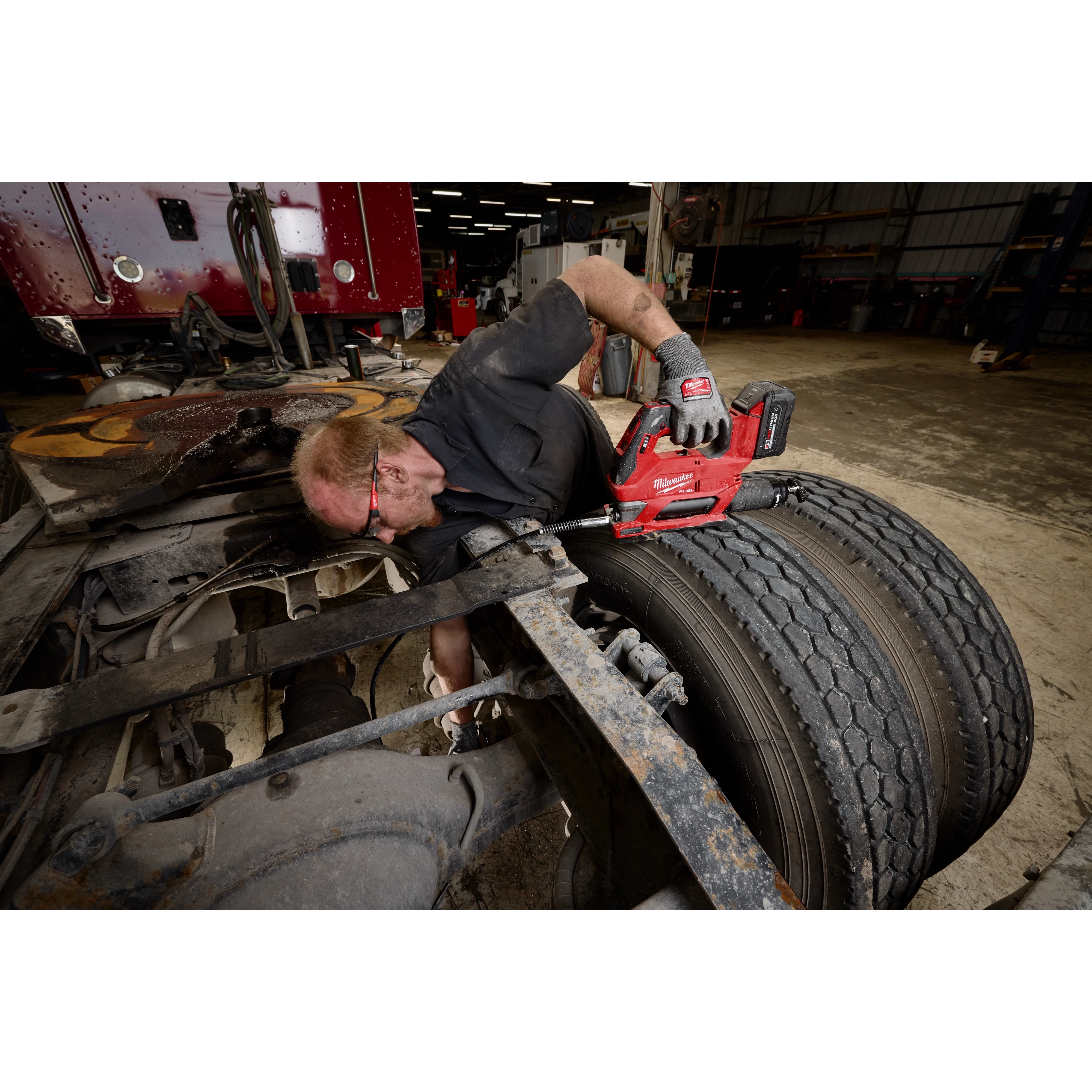 Worker using an M18 FUEL Grease Gun on a truck’s rear wheel assembly in a garage.
