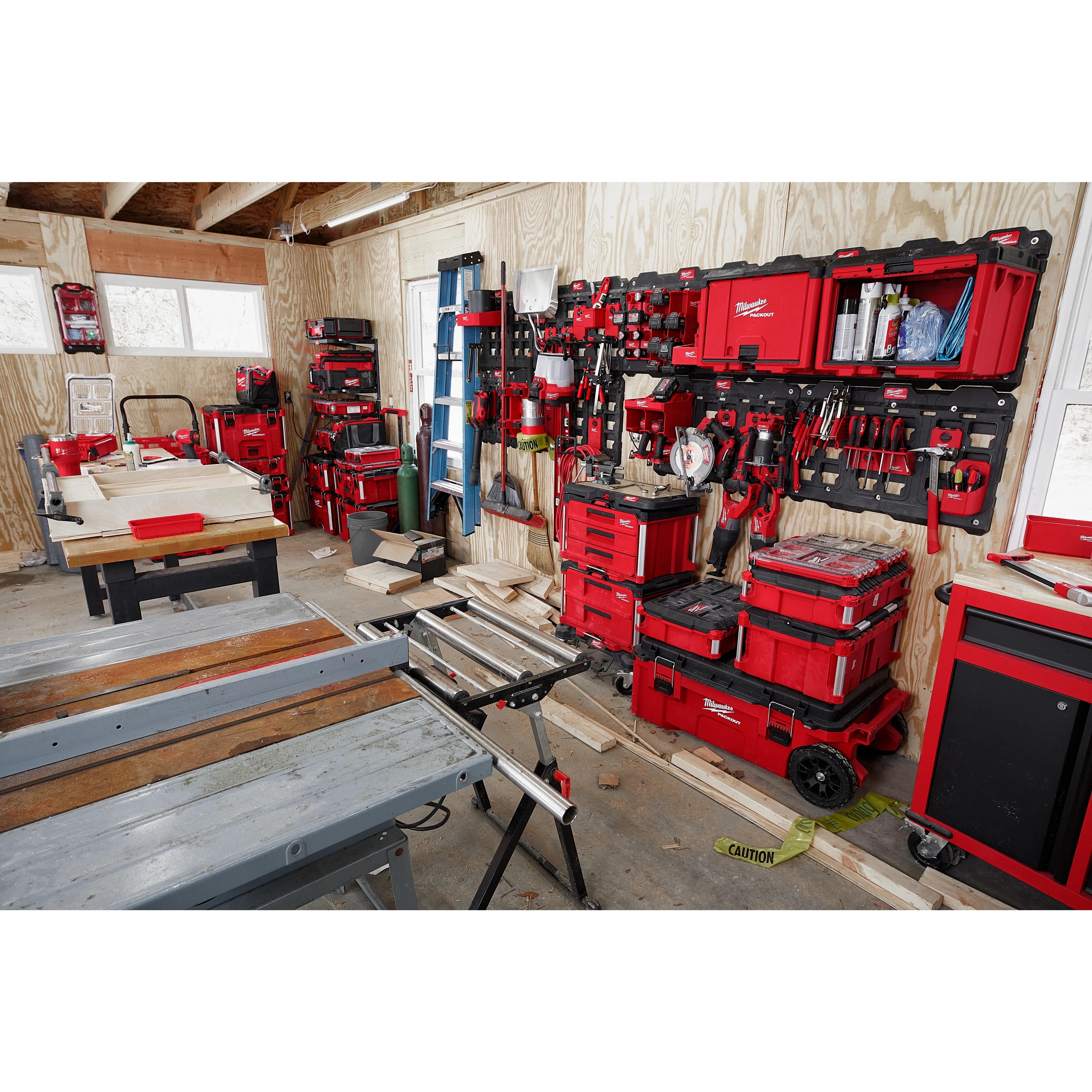 A workshop with tools and equipment organized on red PACKOUT Large Wall Plates, including stacked toolboxes, saws, and hand tools.
