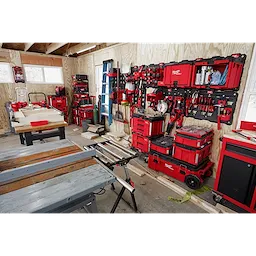 A workshop with tools and equipment organized on red PACKOUT Large Wall Plates, including stacked toolboxes, saws, and hand tools.