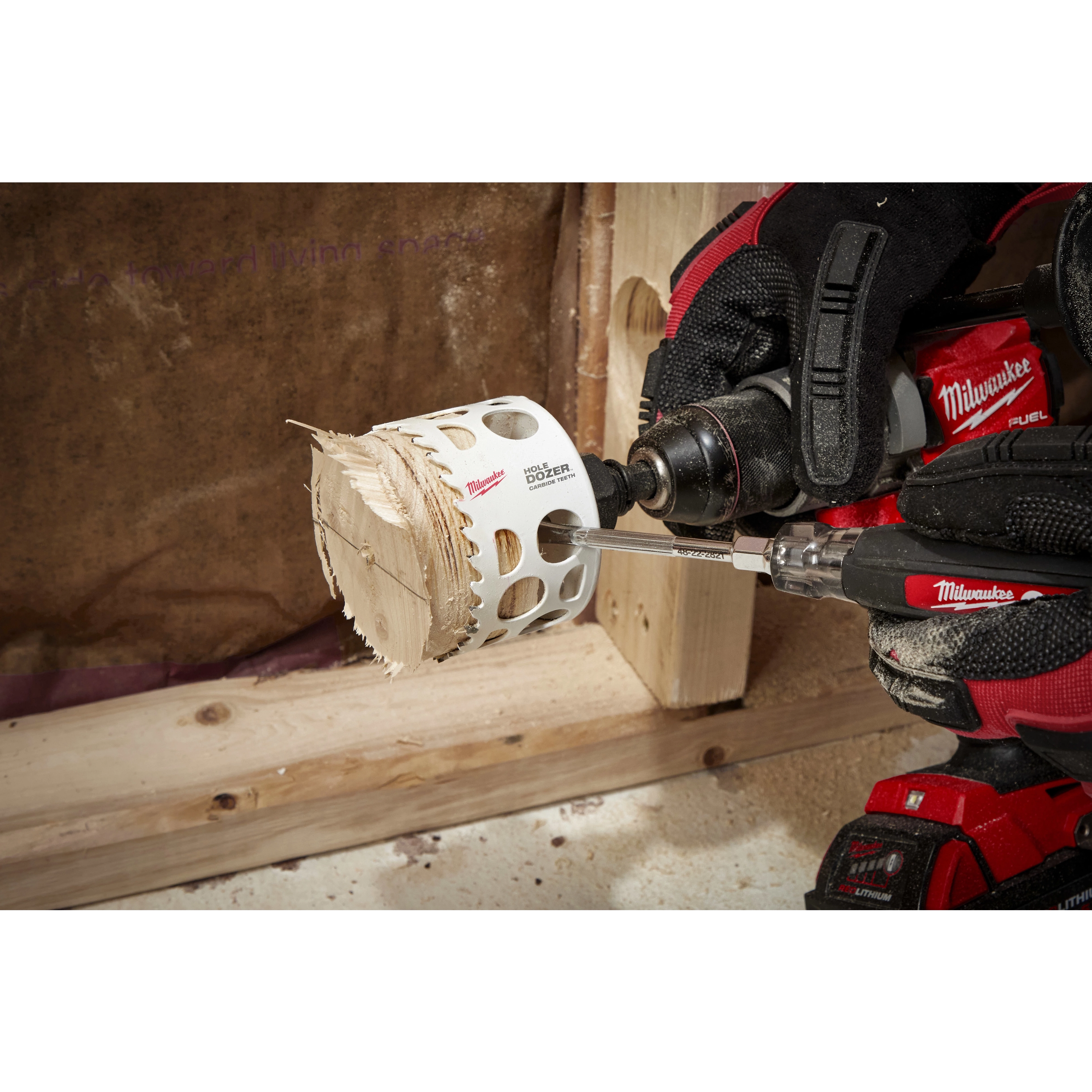 A worker using a drill with a 3-inch Hole Dozer with Carbide Teeth Hole Saw to cut through a wooden board in a workshop.