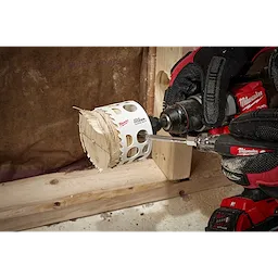 A worker using a drill with a 3-inch Hole Dozer with Carbide Teeth Hole Saw to cut through a wooden board in a workshop.