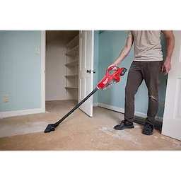 A person vacuums a dusty floor using an M18 Brushless Handheld Vacuum in a partially renovated room.