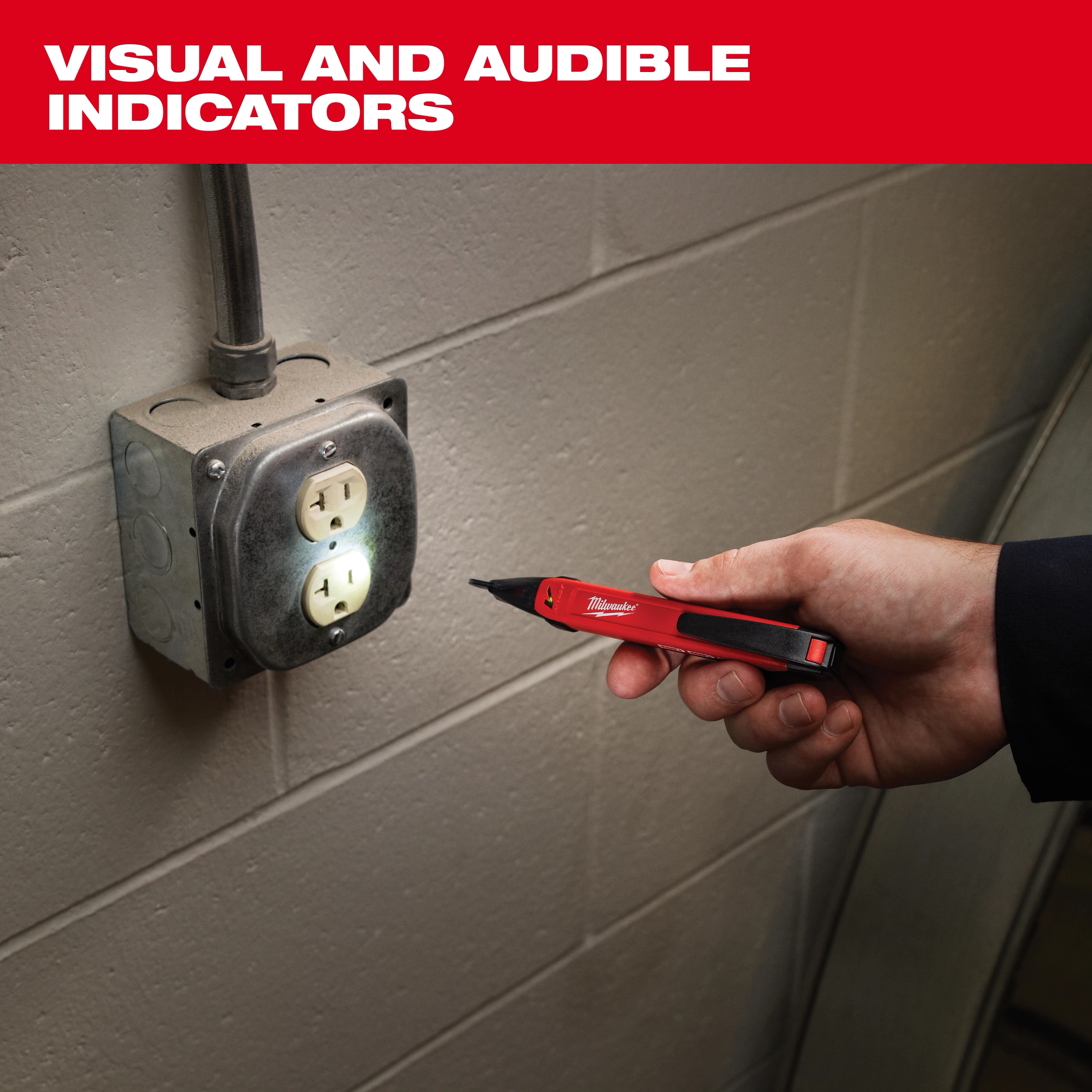 A hand holds a red and black Milwaukee voltage detector next to an electrical outlet on a gray wall. The device lights up, indicating the presence of voltage. The image includes text "VISUAL AND AUDIBLE INDICATORS" in bold white font above the product.