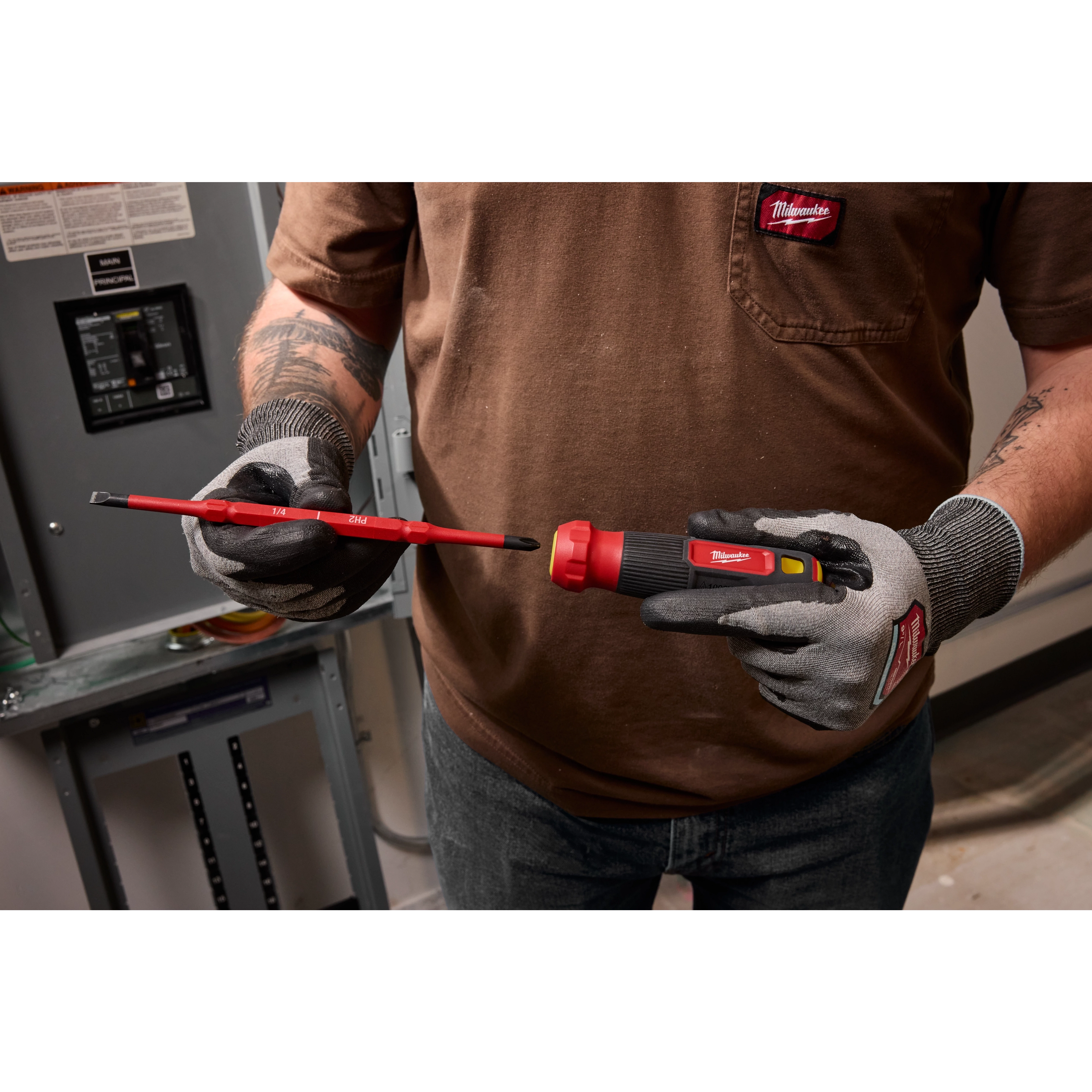A person wearing gloves holds a 2-in-1 1000V Insulated Flip Shank Multi-Bit Screwdriver near an electrical panel, highlighting its flip shank feature.